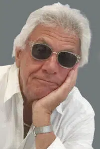 A man with sunglasses on his head and chin resting on one hand.