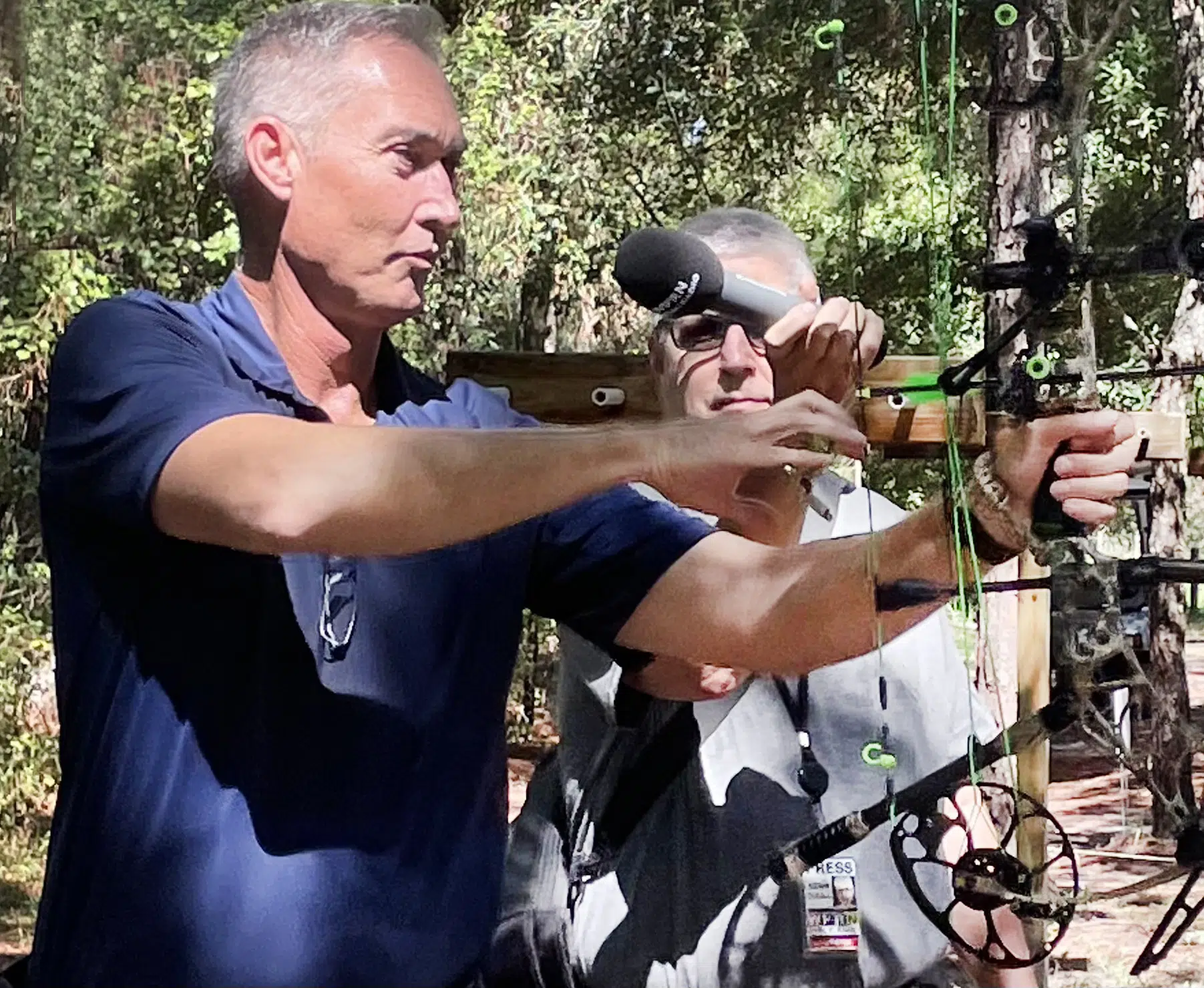 Two men are standing in the woods and one is holding a bow.