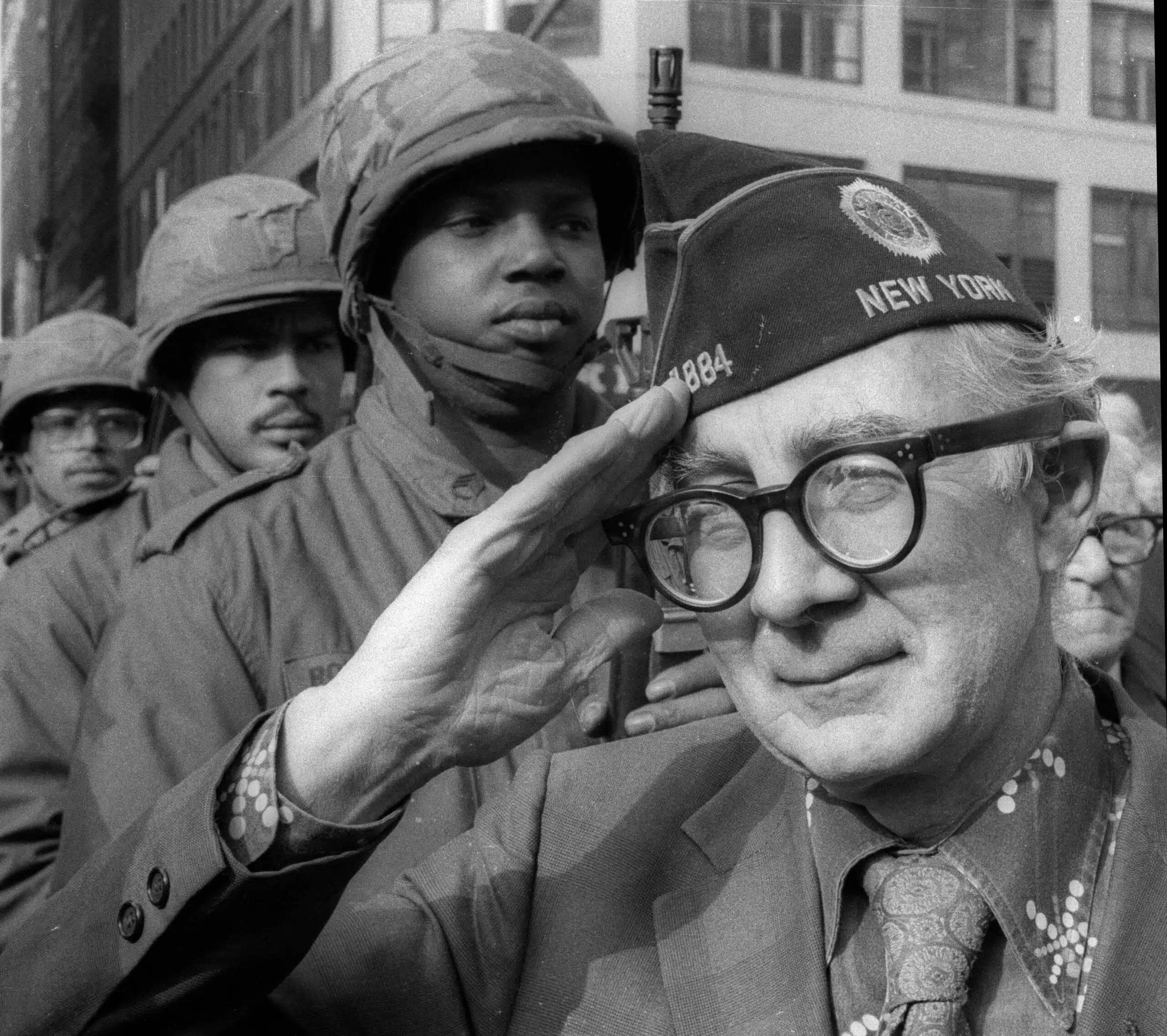 A man in glasses saluting while wearing a hat.