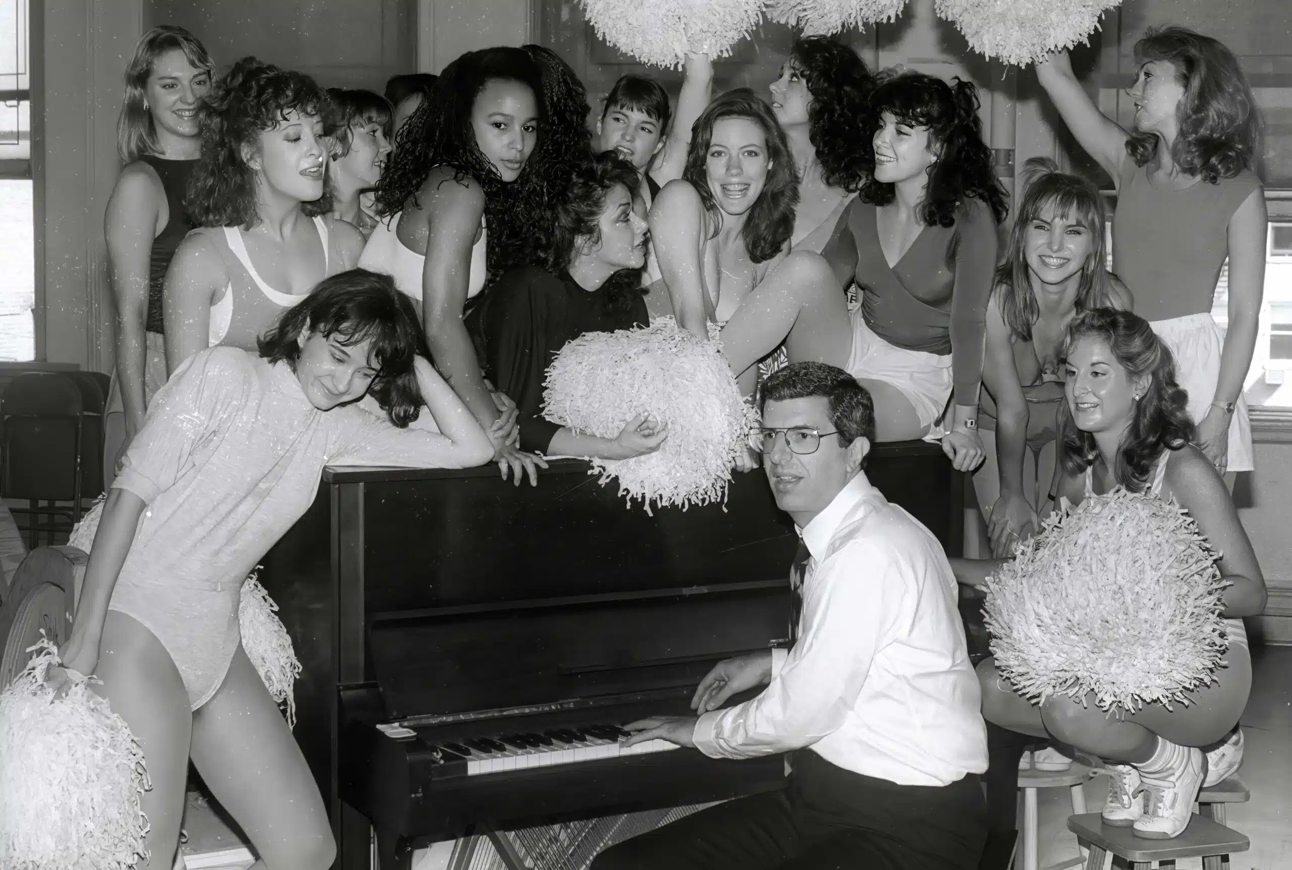 A man sitting on top of a piano surrounded by women.